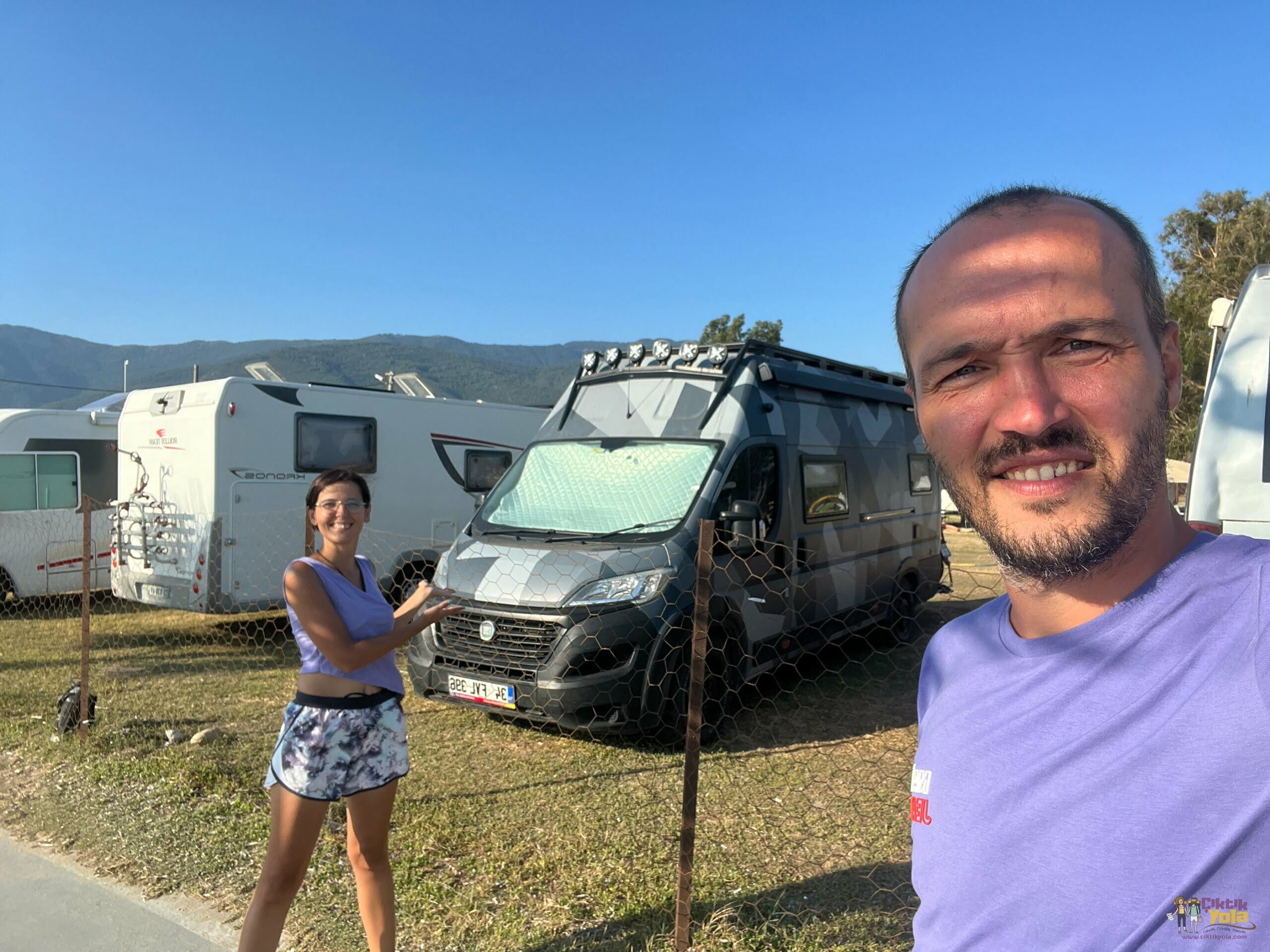 Gri karavanlarının önünde duran iki kişi